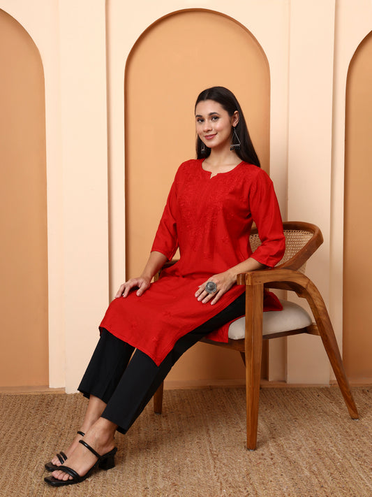 Woman in a red kurta sitting on a chair against a beige wall with arches.