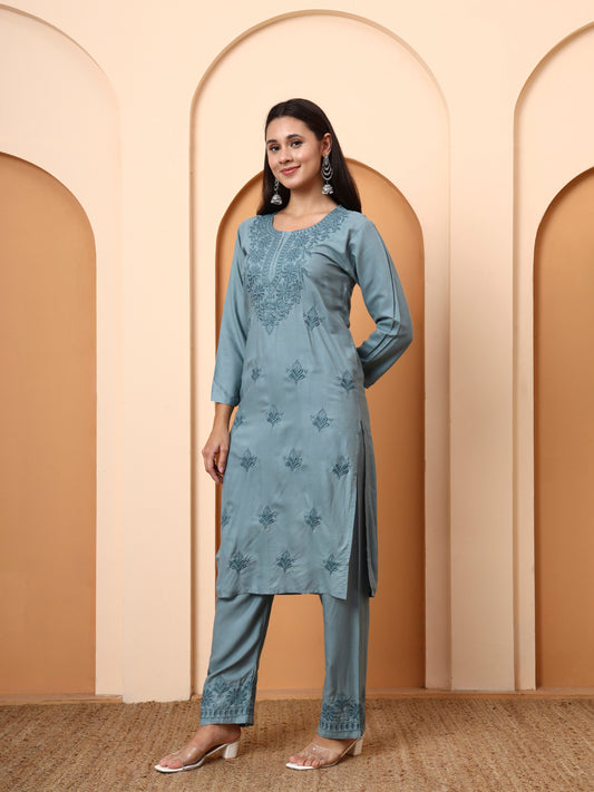 Woman wearing a green embroidered outfit against a beige wall with arches.