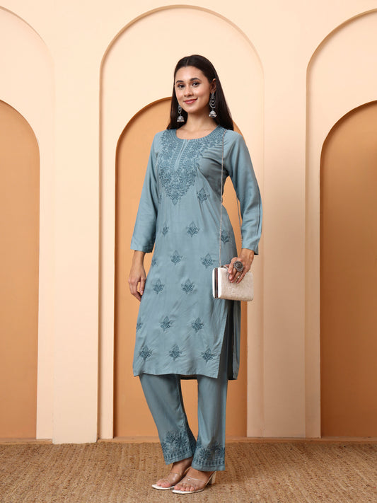 Woman wearing a light green embroidered outfit against a beige wall with arches.